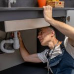 Man carefully examining bottom of sink and pipe